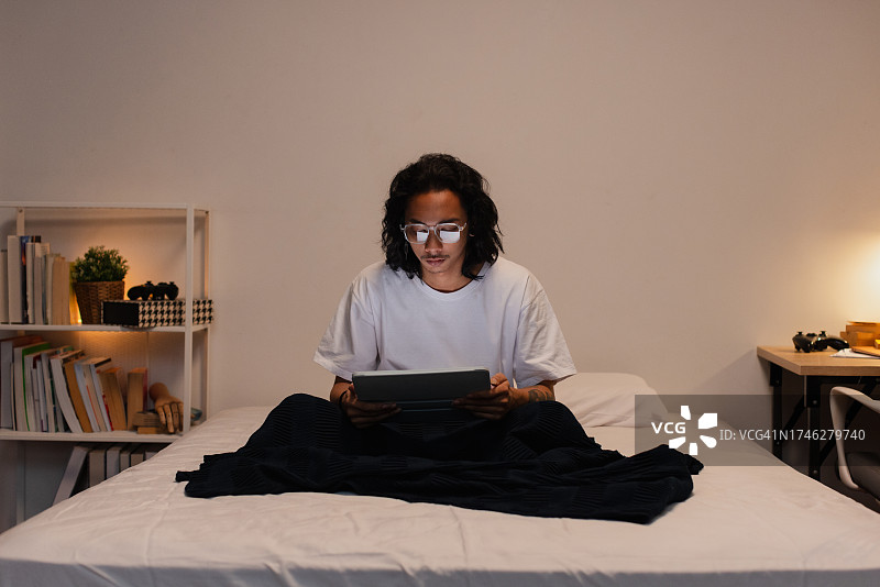 十几岁的男孩在卧室里看平板电脑。图片素材