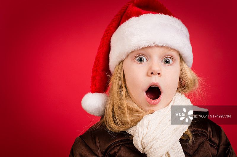 小女孩戴着圣诞老人帽，红色背景图片素材