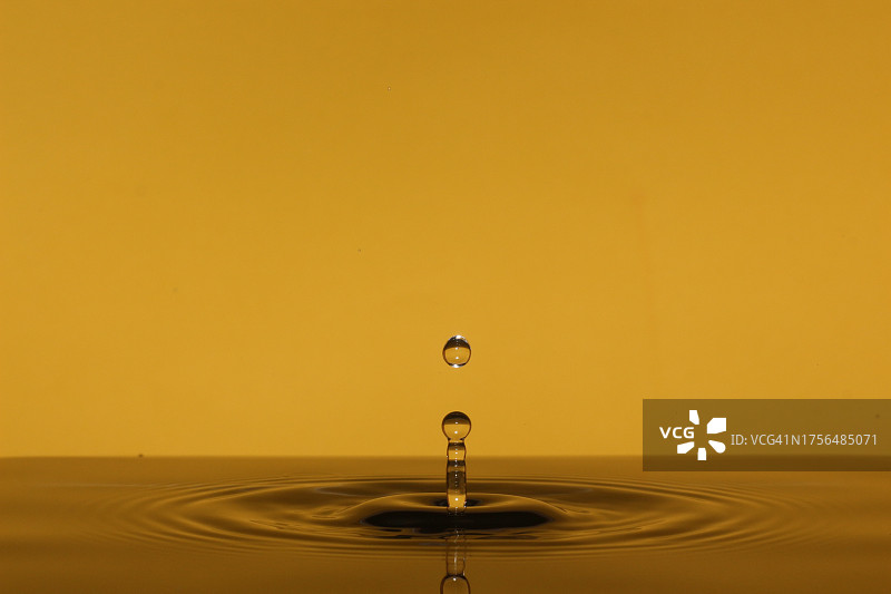 黄色背景下水滴落在水中的特写图片素材