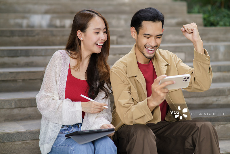 年轻美丽的亚洲女人和聪明的家伙使用高速互联网玩在线游戏与智能手机和数字平板电脑的肖像照片设计艺术品室内城市背景。年轻人都市生活方式科技高速互联网理念。图片素材