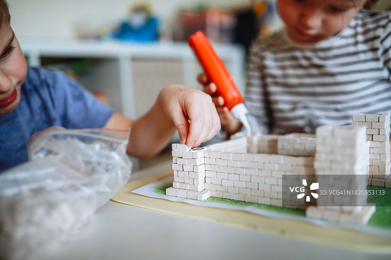 有趣的建筑:孩子们男孩和女孩积极参与用砖块和胶水制作玩具城堡。近距离图片素材