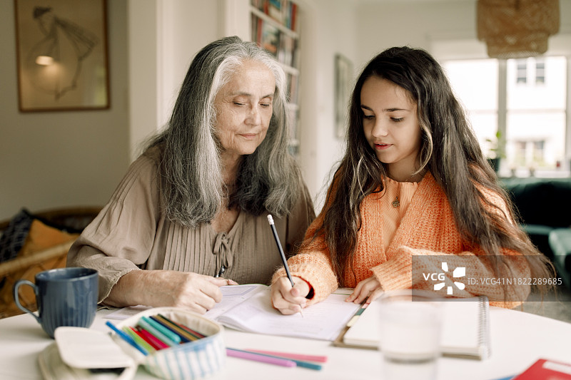 老妇人坐在桌边帮孙女做作业图片素材