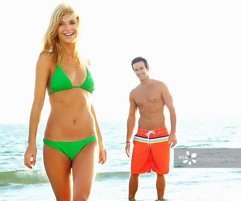 性感的年轻女性在海滩上与一个男人在背景图片素材