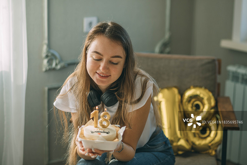 微笑的女人看着生日蛋糕上的18号蜡烛图片素材