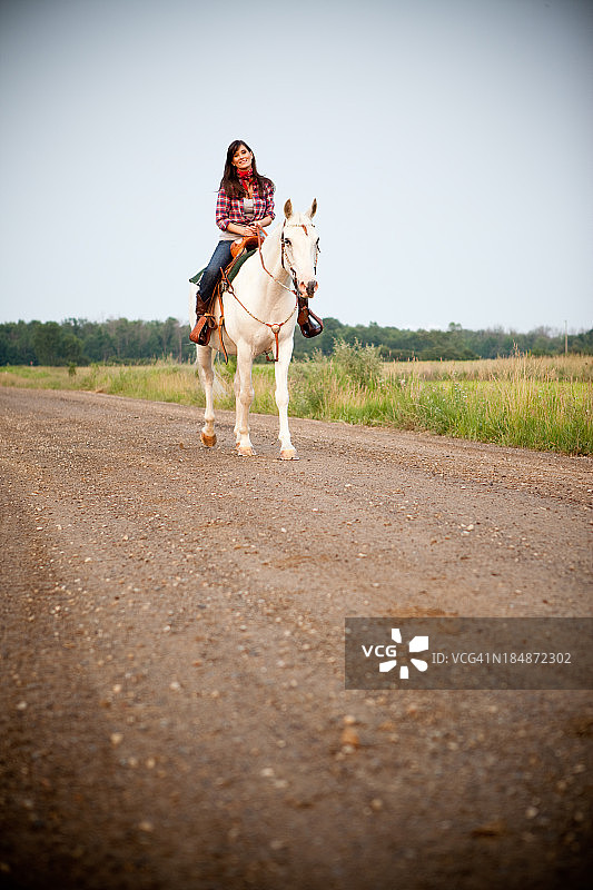 快乐，年轻的女牛仔在乡间路上骑马图片素材