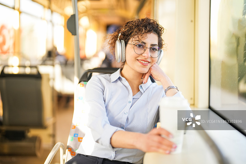 女商人在乘坐公共交通工具时，一边喝咖啡，一边戴着耳机听音乐图片素材