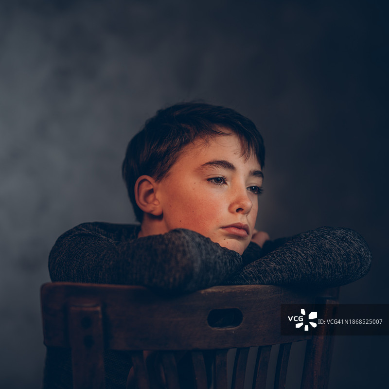 西班牙纳瓦拉，一个男孩坐在黑色背景的椅子上望向别处图片素材