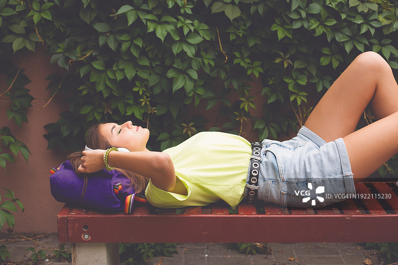 一个十几岁的女孩躺在长凳上听音乐图片素材