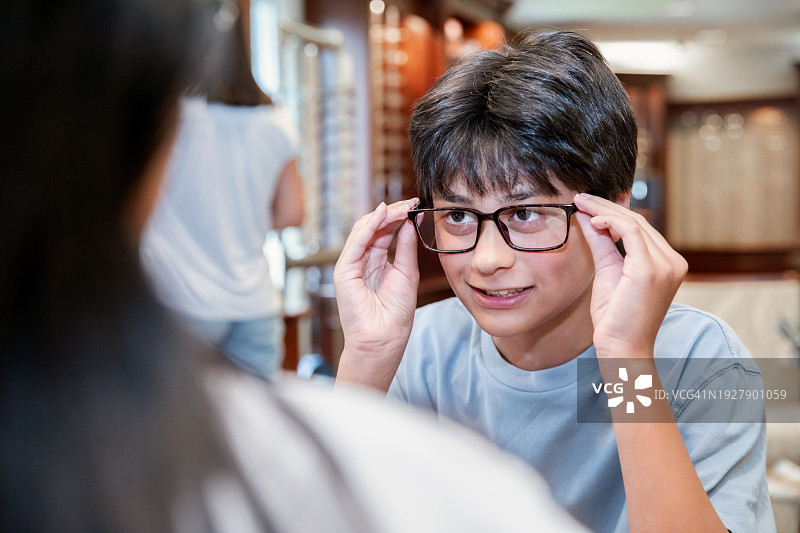 一个十几岁的男孩在眼镜店试穿一副新眼镜。图片素材