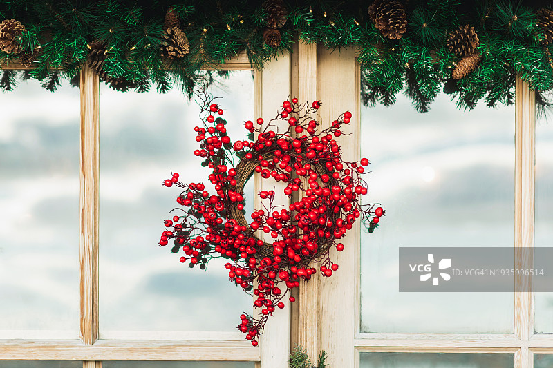 木制窗户上有红色浆果的圣诞花环。图片素材