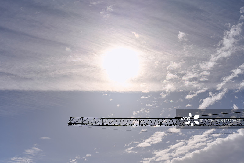 建筑工地金属吊车臂的侧视图，背景是多云的天空。图片素材