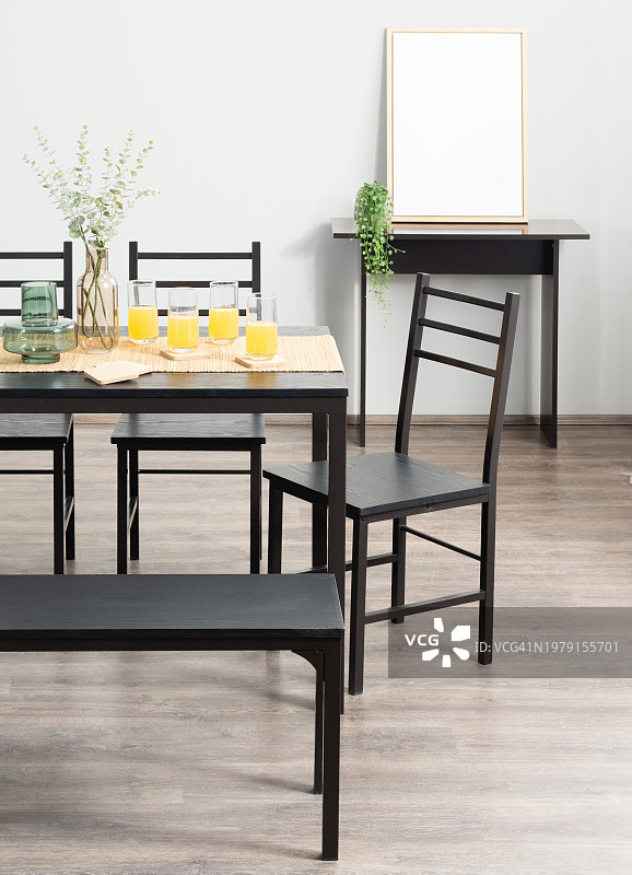 阳光明媚的早晨早餐Nook设有一个黑色的餐椅和长凳，清爽的橙汁在桌子上，一个未经装饰的白色相框，和活泼的绿色植物照亮空间。图片素材