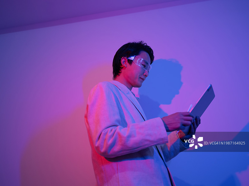 自信的亚洲商人在霓虹灯下使用数码平板电脑图片素材