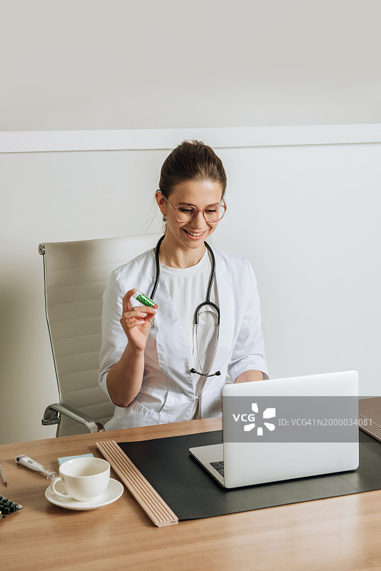 一名女医生手里拿着一罐药丸，通过笔记本电脑利用互联网技术在线咨询病人。图片素材