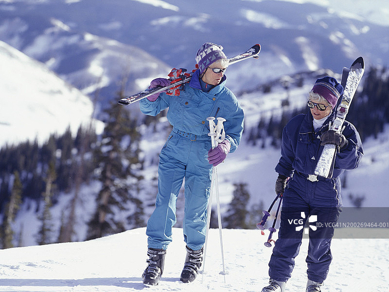 两个女人背着滑雪板在山上行走图片素材