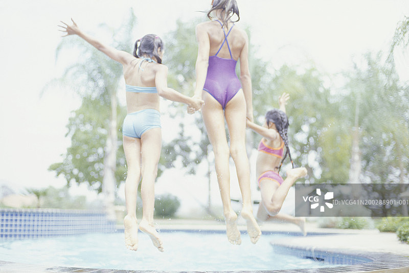 三个女孩(6-7)(8-9)(12-13)跳进泳池，后视图图片素材