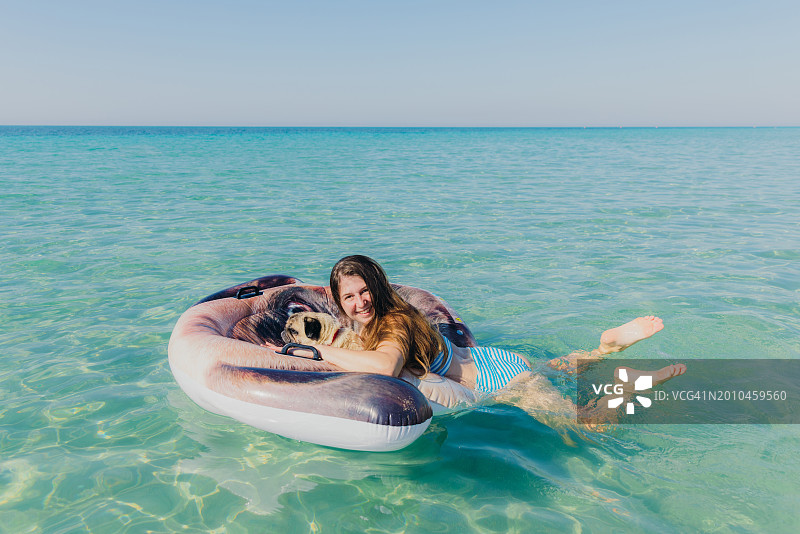 意大利普利亚，一个快乐的女人和她的狗一起漂浮在海上图片素材