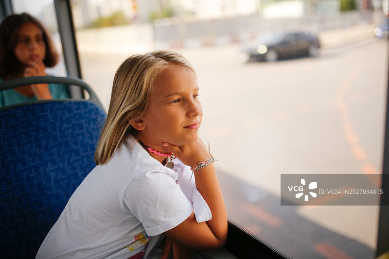 小女孩在城市里乘公共汽车时望向窗外。图片素材
