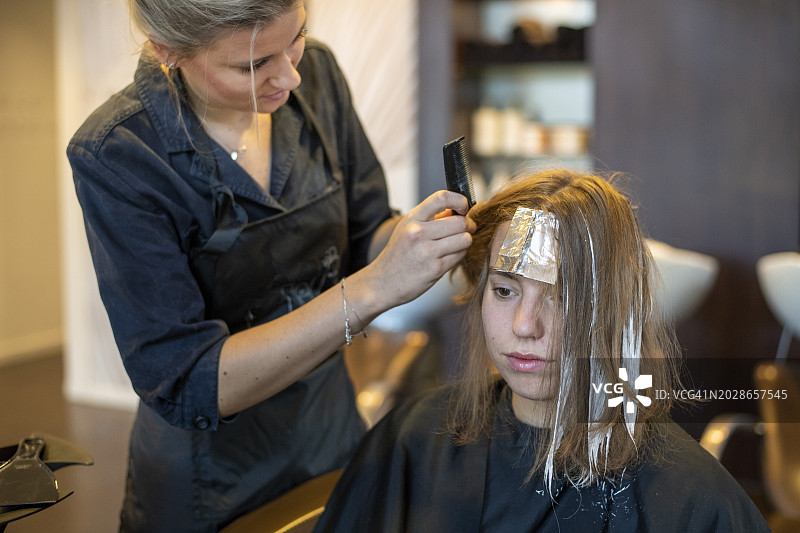 迷人的金发模特正在做她的头发，由专业的发型师在她染发和做头发的时候给她做了一个放松的发型图片素材