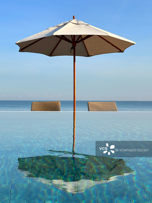 一个太阳伞和两个太阳躺椅在海边游泳池的反射图片素材