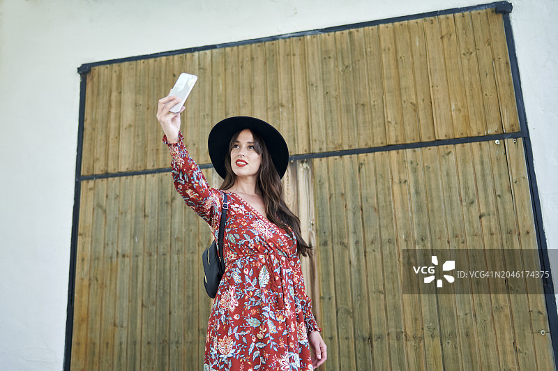 戴帽子的女子在木门前用手机自拍图片素材