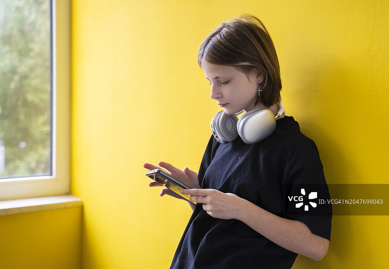 戴着无线耳机的女孩在家里的黄墙边使用智能手机图片素材