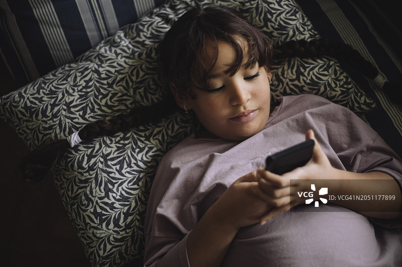 女孩躺在家里的床上使用智能手机的高视角图片素材