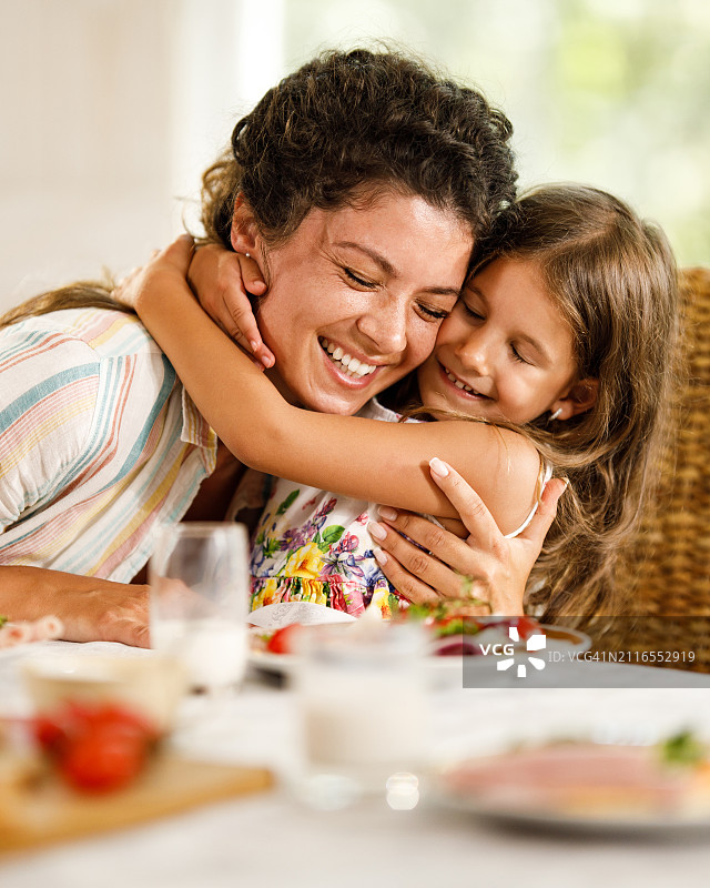 幸福的单身母亲和女儿在家里吃早餐时拥抱在一起。图片素材