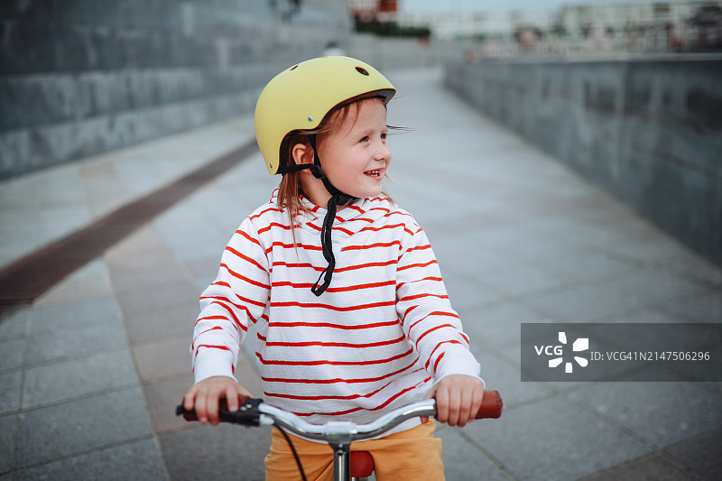 戴着头盔的孩子骑着平衡自行车在城市的灰色长廊上享受骑行图片素材