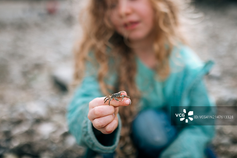 在沙滩上玩耍的女孩展示着她抓到的小螃蟹图片素材
