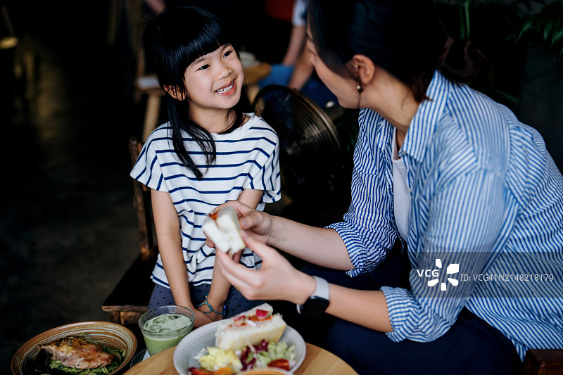年轻的亚洲母亲和她可爱的女儿在咖啡馆享受美味的三明治和意大利面。他们聊天，享受他们在一起吃饭的时间。母女亲密时刻。家庭生活方式，一起出去吃饭图片素材
