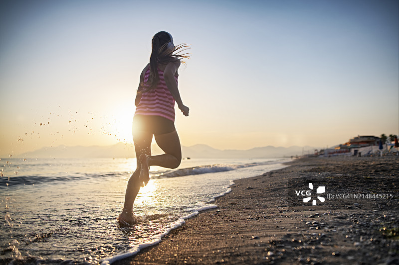 一个阳光明媚的夏日，一个十几岁的女孩在沙滩上慢跑图片素材