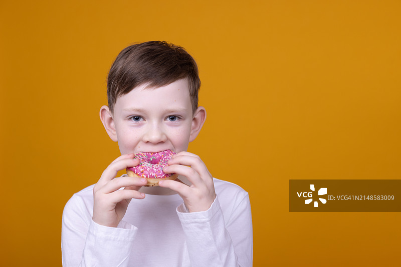 酷酷的金发男孩拿着甜甜圈微笑着在黄色背景上玩耍图片素材