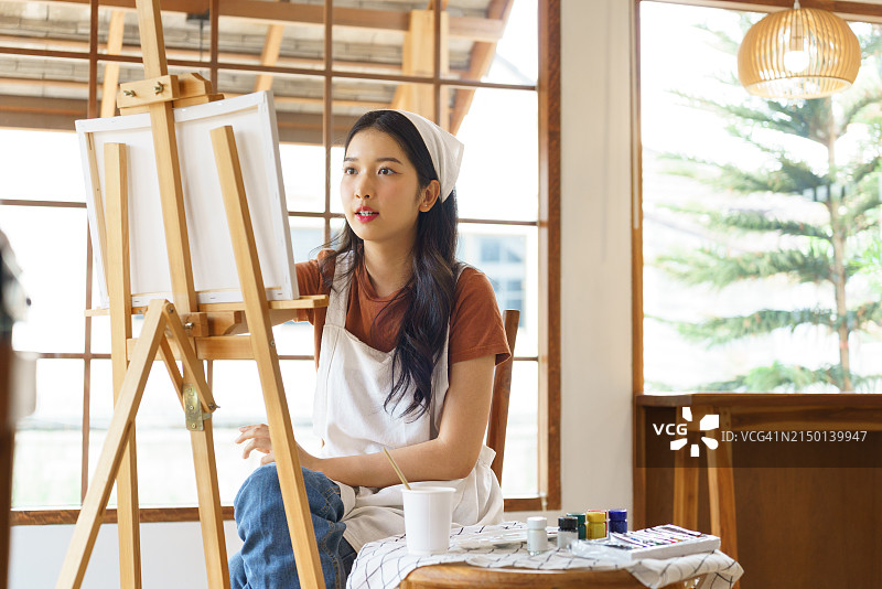 年轻的亚洲艺术家女性在工作室里以艺术爱好的生活方式创作艺术品，同时思考着设计创意杰作和在画架上绘制画布的想法图片素材