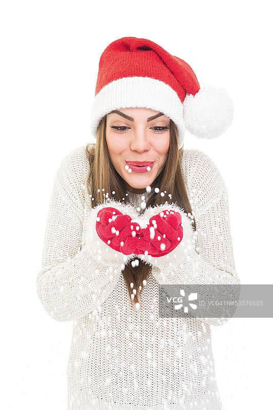 快乐的年轻女子戴着圣诞帽吹雪图片素材