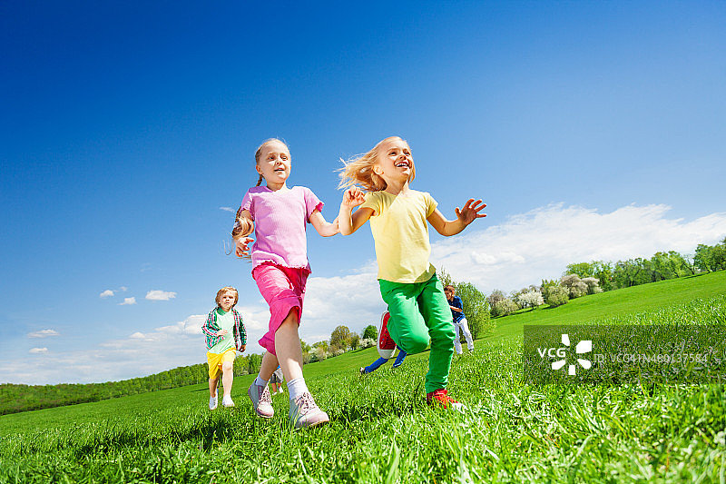快乐的女孩和其他孩子在绿色的田野里奔跑图片素材