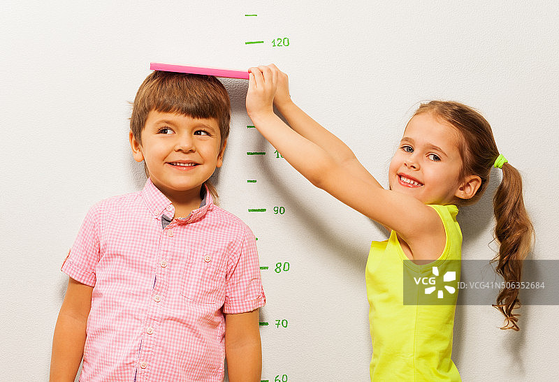 男孩和女孩在家用墙秤测量身高图片素材