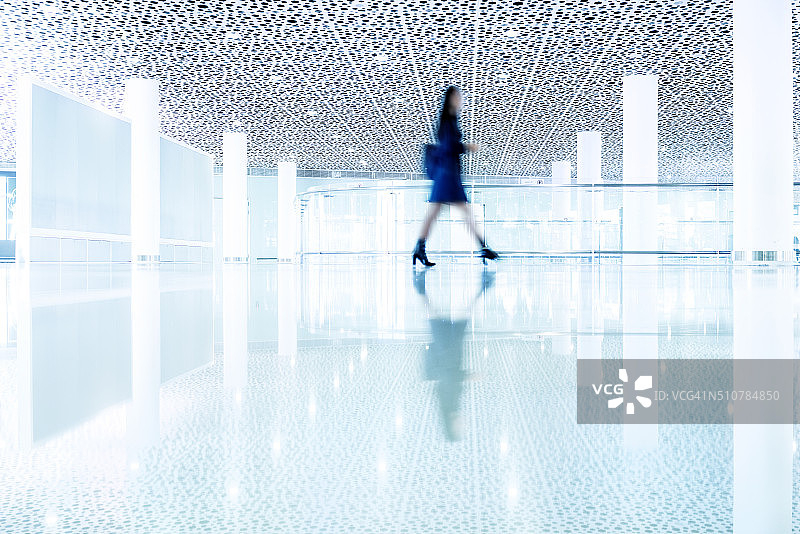 动作模糊的女人走在现代化的机场走廊上图片素材