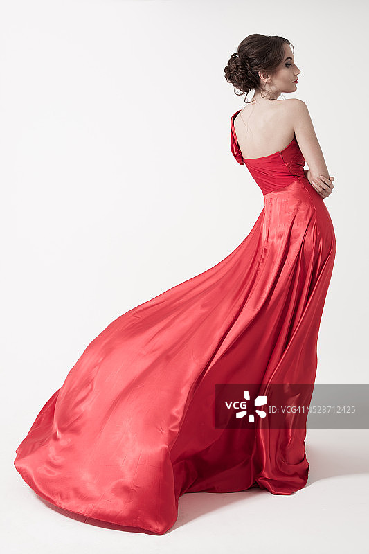 穿着飘动的红裙子的年轻美女。白色背景。图片素材
