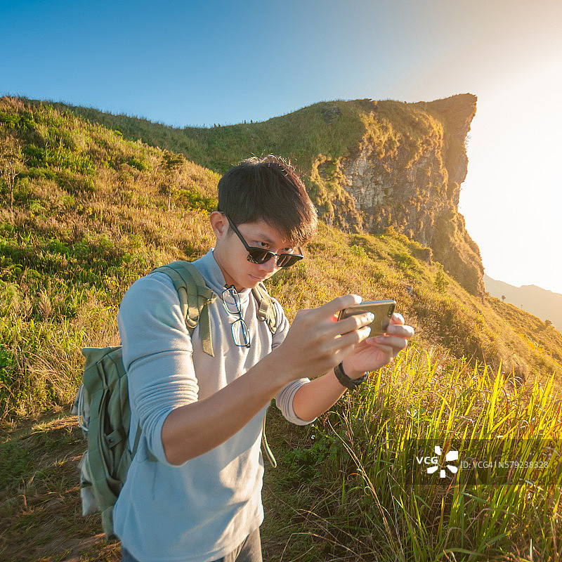 年轻的旅行者站在山上望着夕阳。图片素材