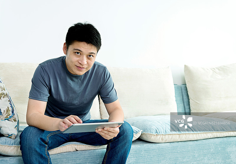 一个年轻人坐在沙发上使用平板电脑图片素材