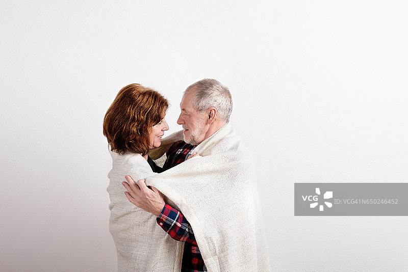 老夫妇拥抱着，裹在白色的毯子里。影棚拍摄。图片素材