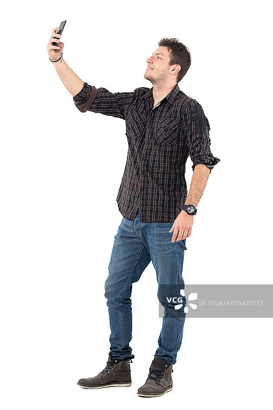穿着牛仔裤和格子衬衫的休闲男子用手机拍照。图片素材