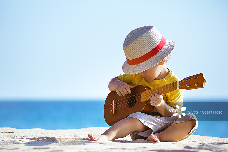小男孩在海滩上弹吉他尤克里里图片素材