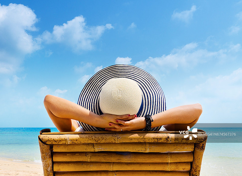戴着帽子的女人在海滩上放松，看着大海。副本的空间。图片素材