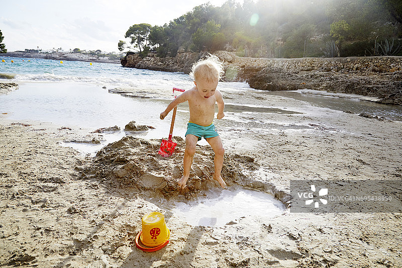 蹒跚学步的孩子跳进沙滩上的水坑里图片素材