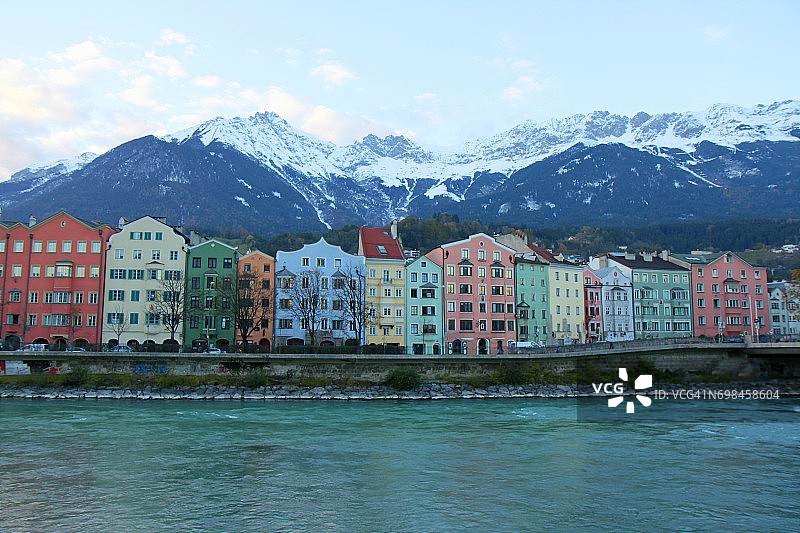 在奥地利，因斯布鲁克酒店的河岸建筑立面和田园诗般的北蒂罗尔雪山覆盖的卡温德尔山脉的日出图片素材