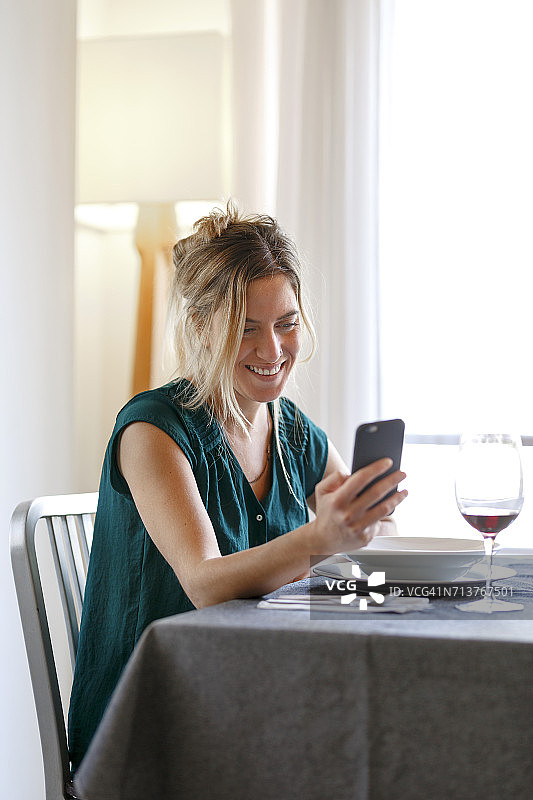 女人坐在餐桌旁，微笑着用智能手机图片素材