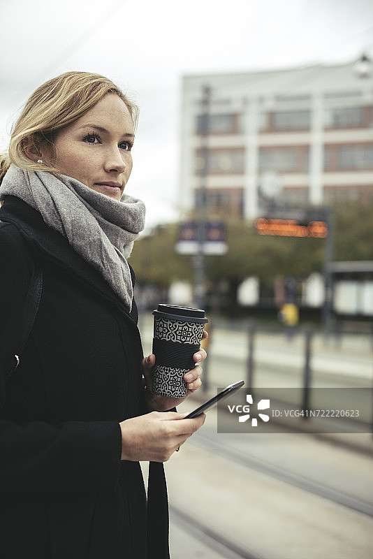 在电车站拿着智能手机和一次性咖啡杯的女商人图片素材