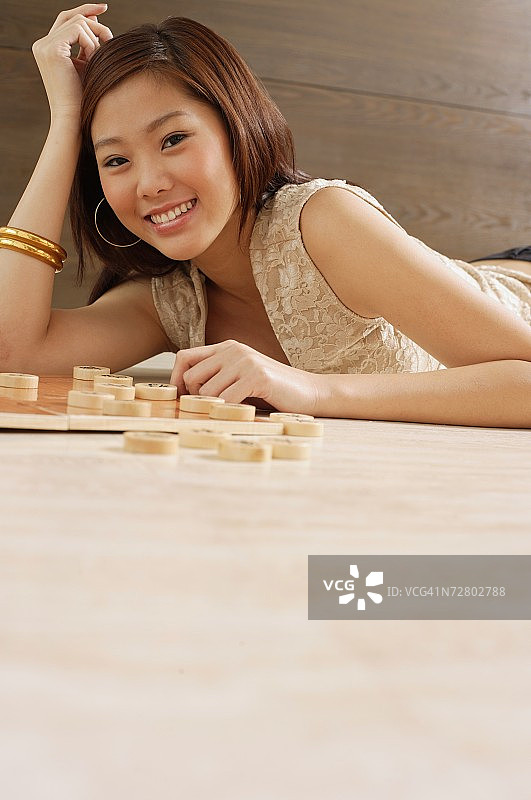 女人躺在地板上，手放在头上，中国棋子在她旁边的地板上图片素材